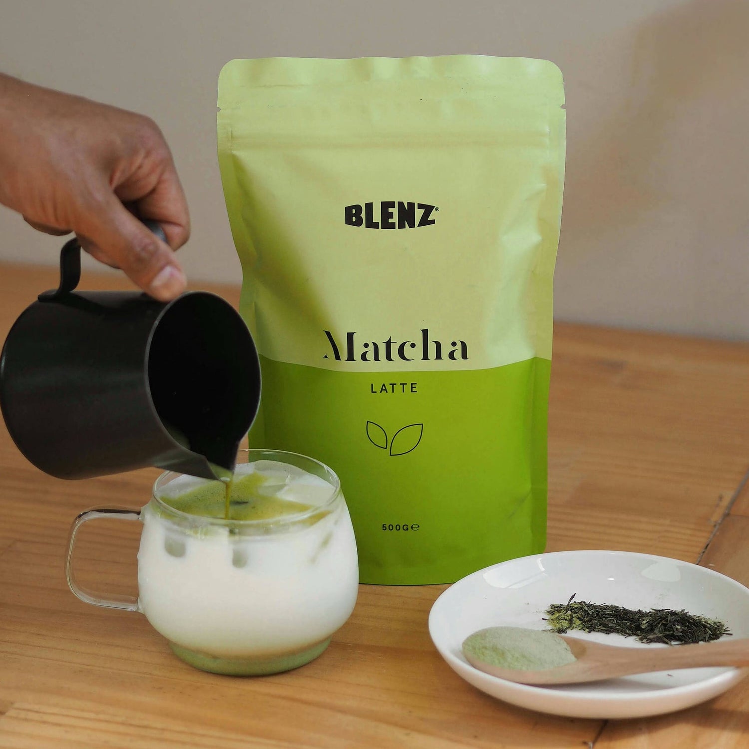 Matcha powder in bag and an iced latte being poured with milk jug