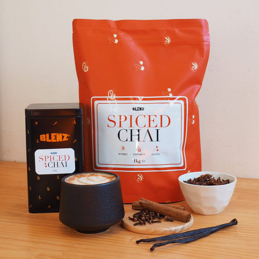 Spiced Chai powder in bag and tin next to latte art on cafe bench