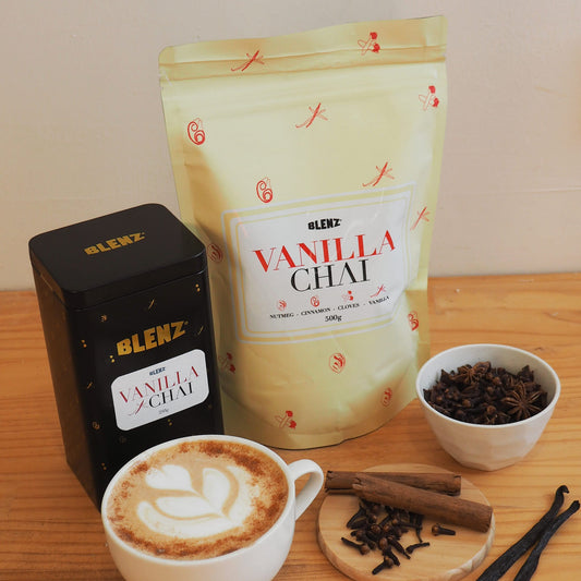 Vanilla chai powder in bag and tin next to chai latte on cafe bench