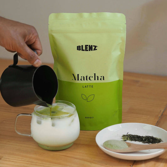 Blenz Matcha powder 500g bag and iced latte on cafe bench with barista pouring